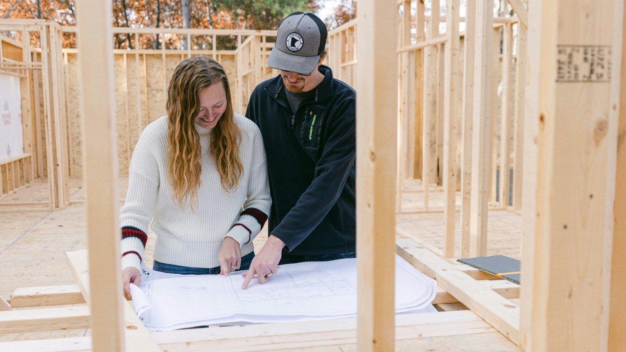 Couple reviewing blueprints inside a home under construction